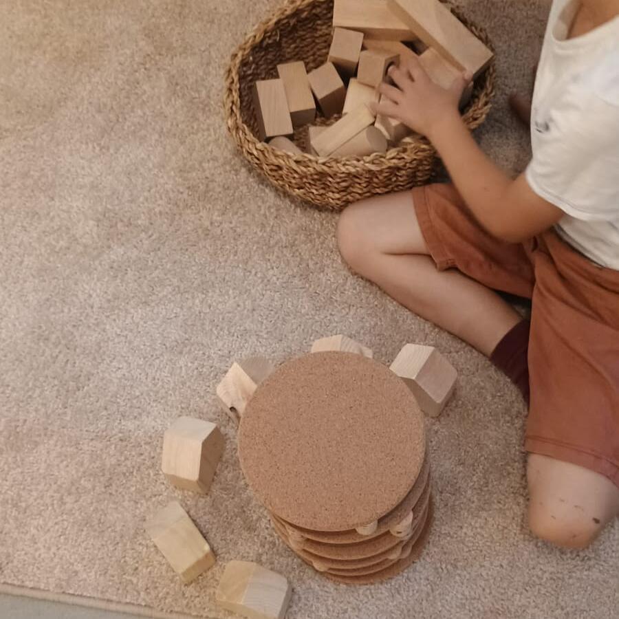 Kinderhand spielt mit einem Korb voller runder Holzscheiben auf dem Boden