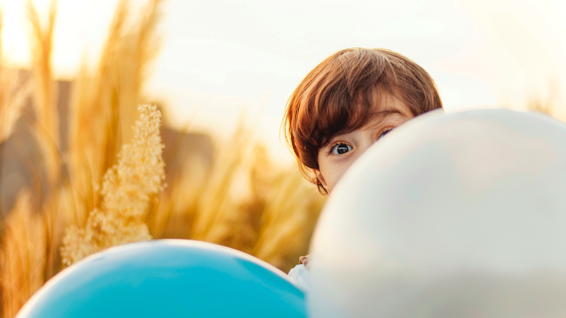 Kind schaut hinter Luftballons hervor