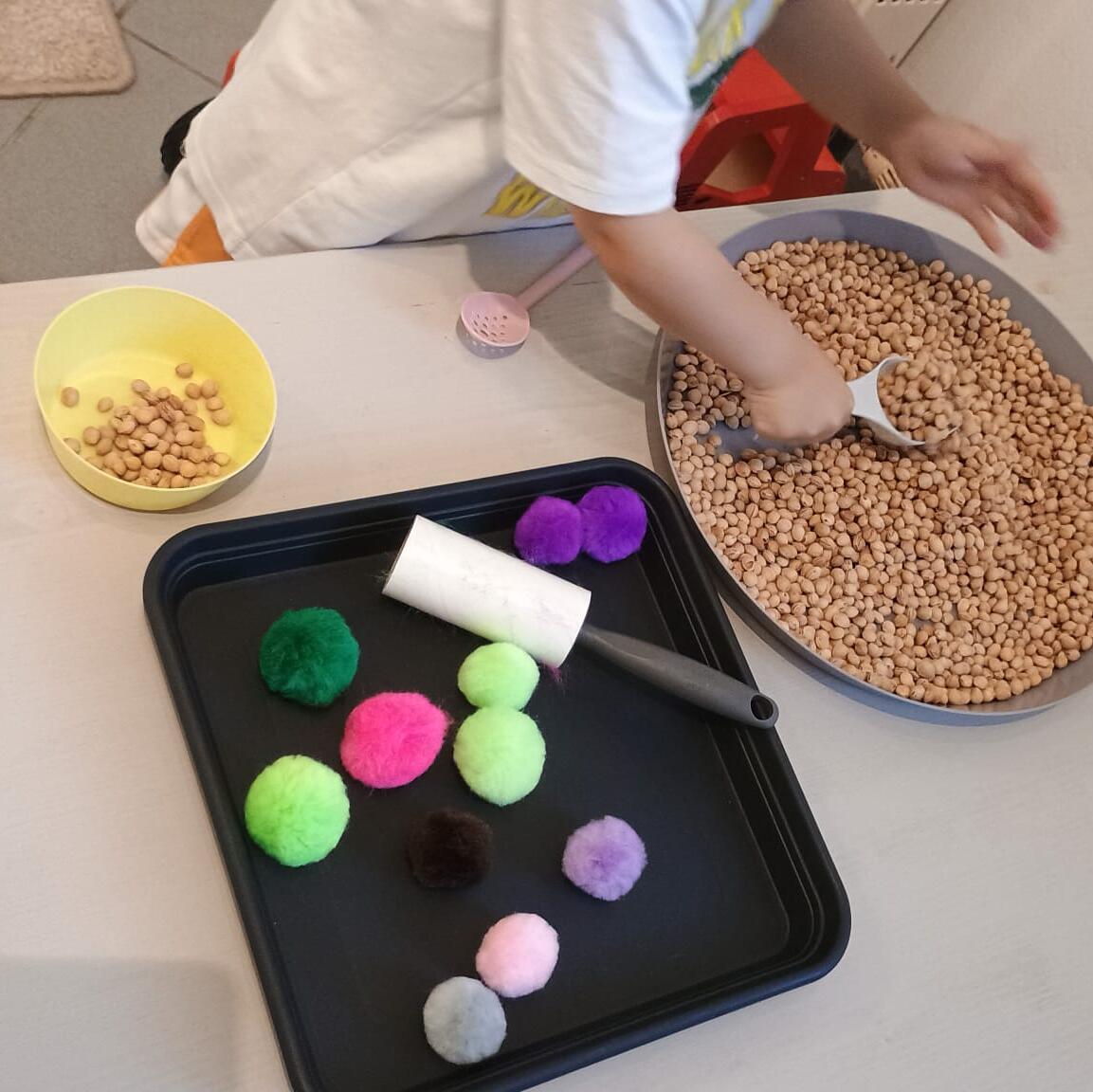 Kinderhand greift nach bunten Knöpfen neben einer Schüssel Kichererbsen bei einem Sortierspiel