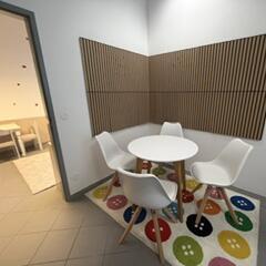 Sitzecke mit rundem weißen Tisch und Stühlen vor einer Wand mit Holzlamellen-Verkleidung